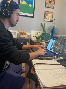 A student sits at a desk and types on a laptop while wearing headphones.